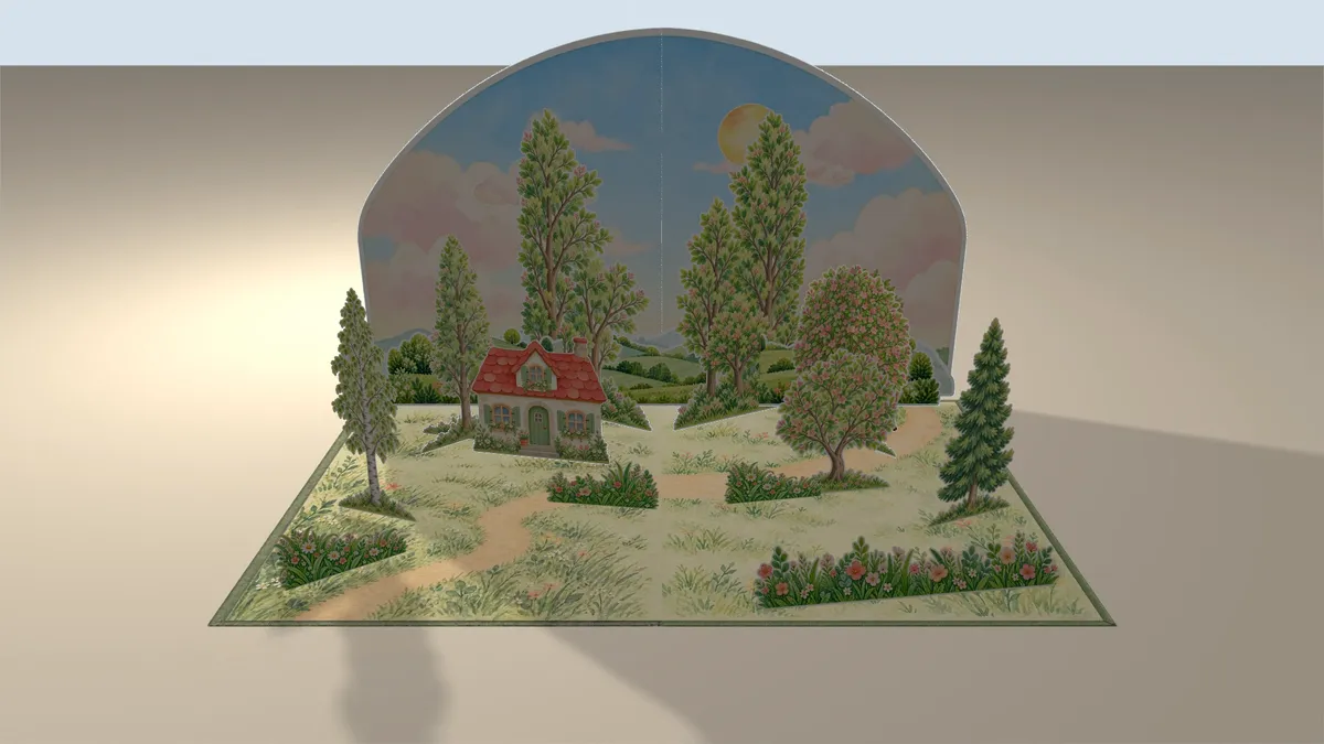 Pulled back: the whole pop-up spread with its sky card, trees and cottage standing on an open book on a table, its shadow behind it